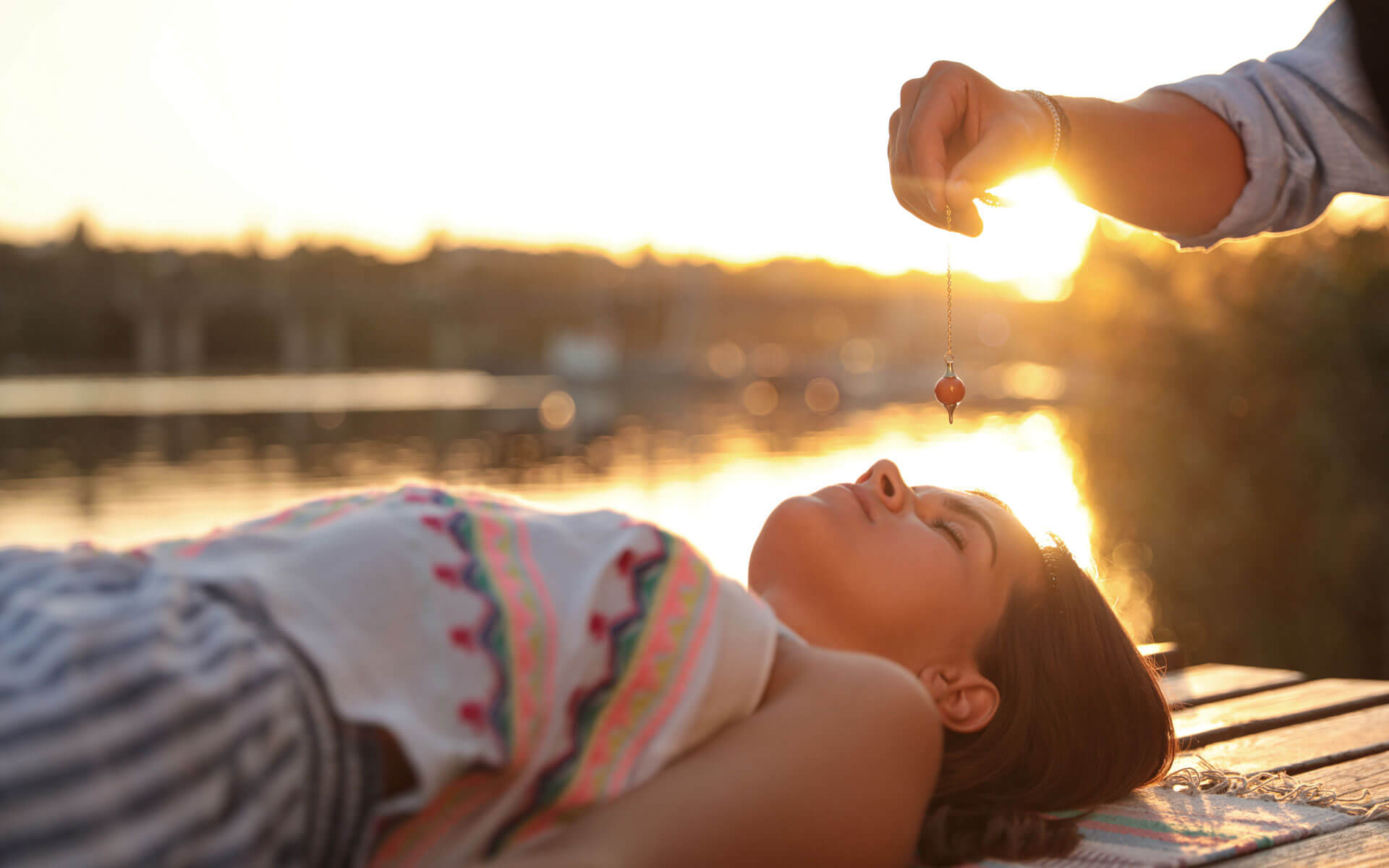 Woman lying down receiving energy healing with a pendulum over her third eye